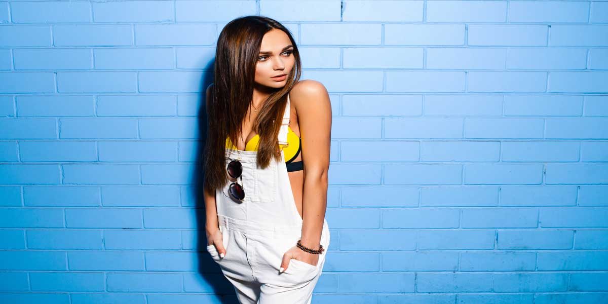 Image Commercially Licensed from https://depositphotos.com/photo/beautiful-young-sexy-hipster-girl-posing-and-smiling-near-urban-blue-wall-background-in-yellow-111722706.html